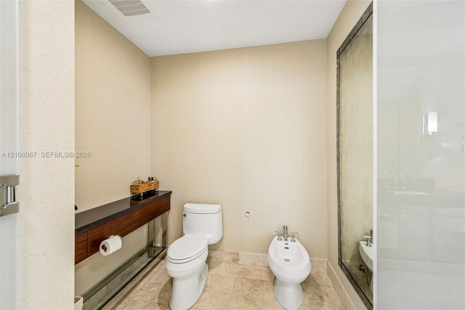 Wall-mounted wood-finish vanity with a dark stone countertop, stone tile flooring, toilet, and bidet