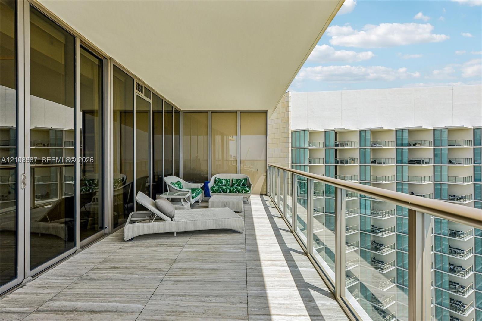 Expansive private balcony featuring large-format tile flooring, a glass-panel railing with a metal frame, and floor-to-ceiling glass sliding door panels