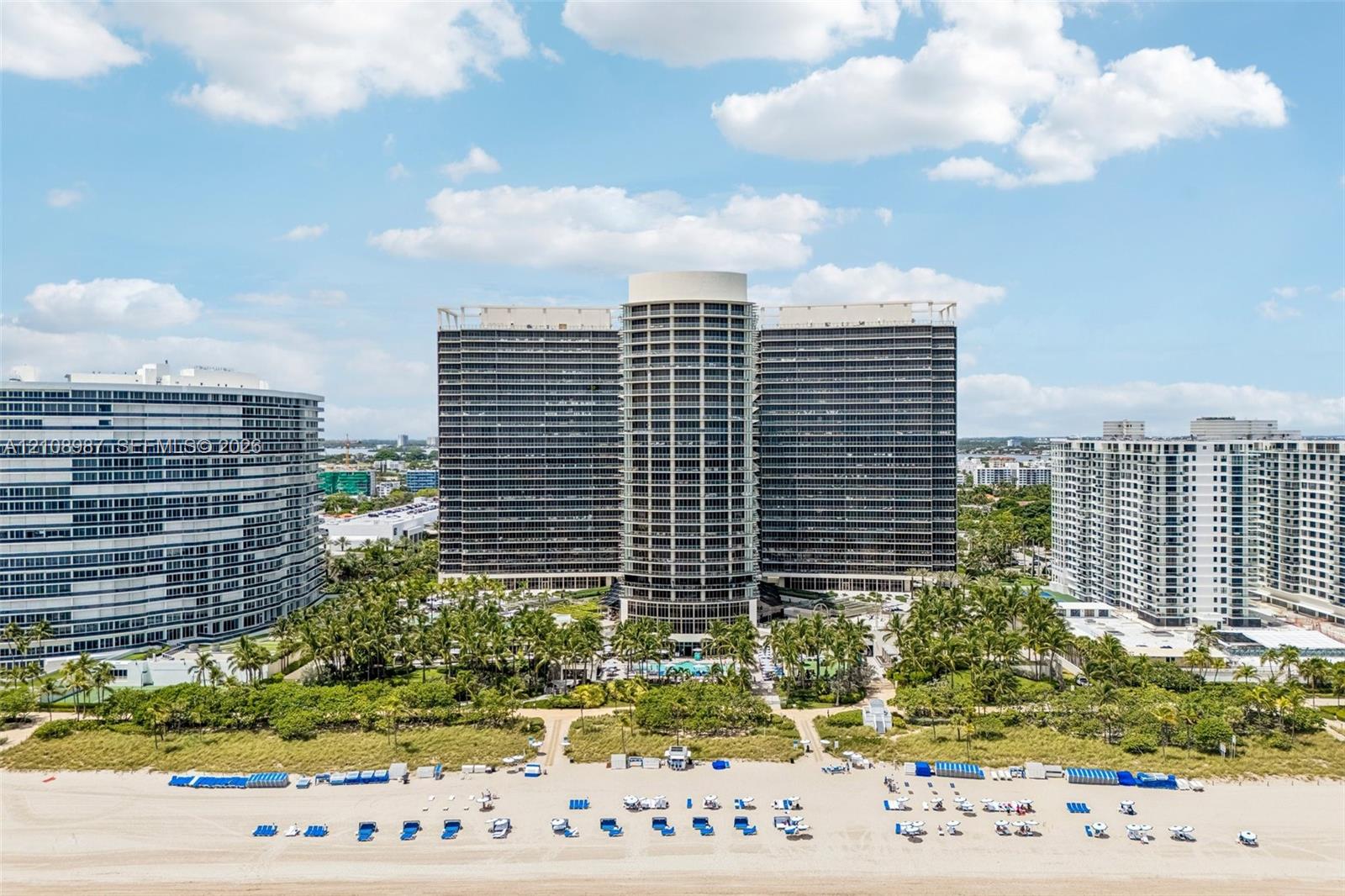 High-rise residential exterior featuring expansive glass balcony facades, a centered cylindrical architectural design, and direct coastal frontage