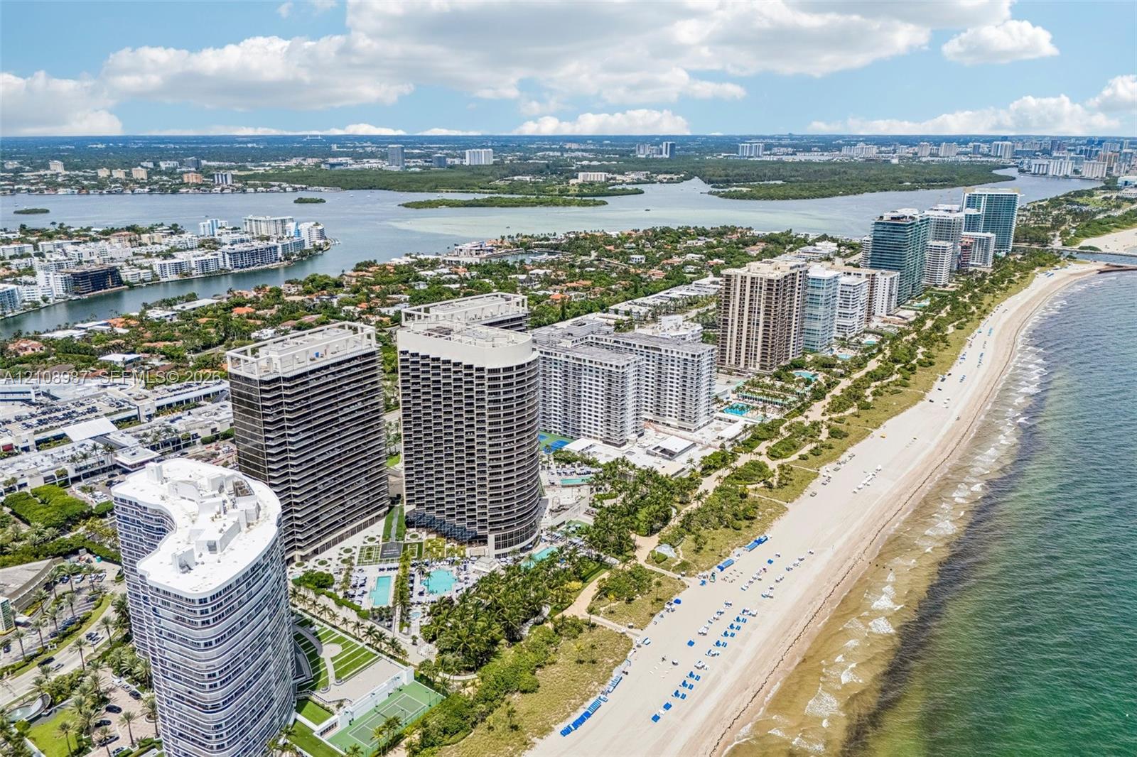 Aerial perspective of coastal high-rise towers featuring direct beach access, outdoor swimming pools, and dedicated tennis courts situated along the shoreline