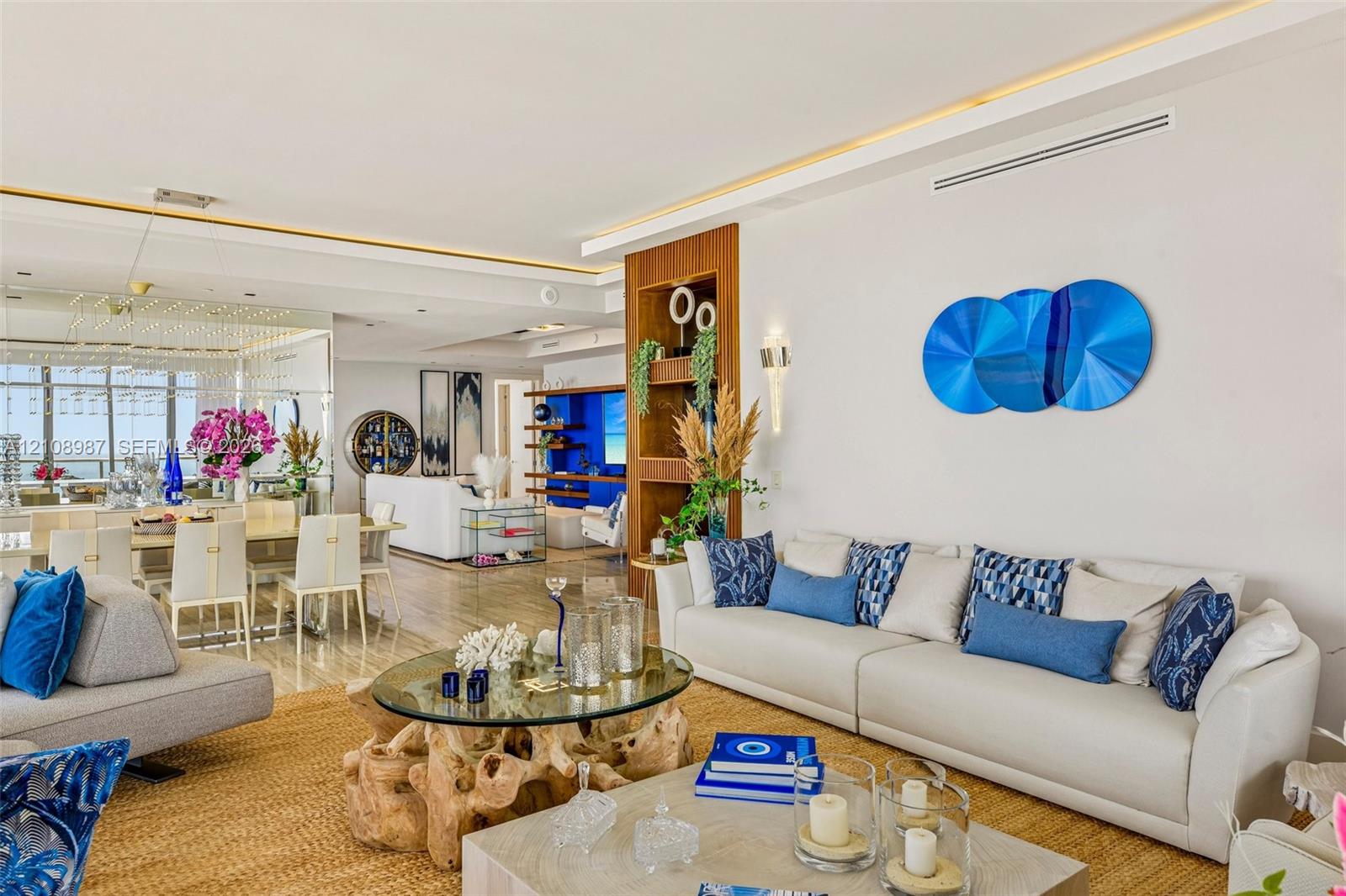 Open-concept interior featuring recessed cove lighting, built-in floor-to-ceiling wood shelving, mirrored wall paneling, and wood-finish flooring