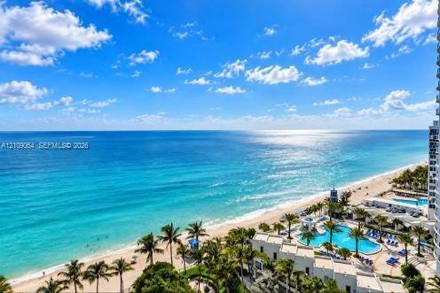 High-altitude perspective featuring an expansive ocean horizon, sandy coastline, and a multi-pool aquatic complex with surrounding palm trees