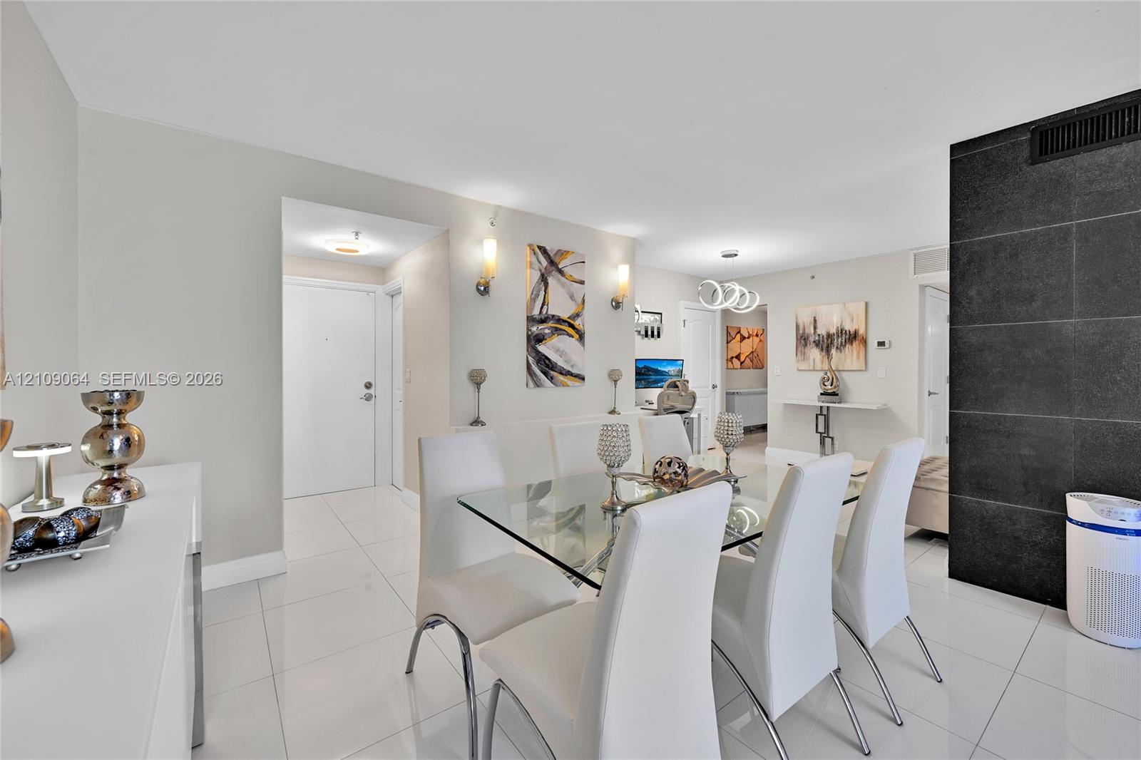 Galley kitchen featuring wood cabinetry, stone-surface countertops with matching backsplashes, stainless steel appliances, polished tile flooring, and a contemporary architectural light fixture