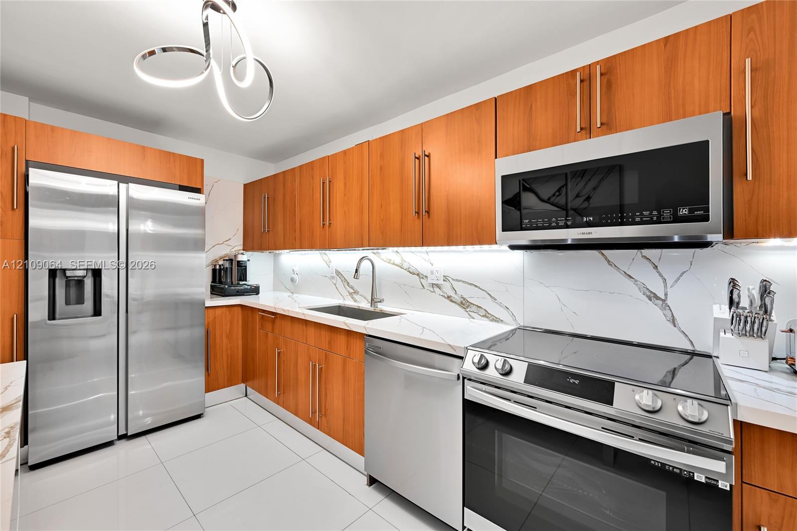 Open-concept space featuring polished tile flooring, a modern multi-ring sculptural chandelier, wall-mounted ambient sconce lighting, and a built-in recessed storage niche