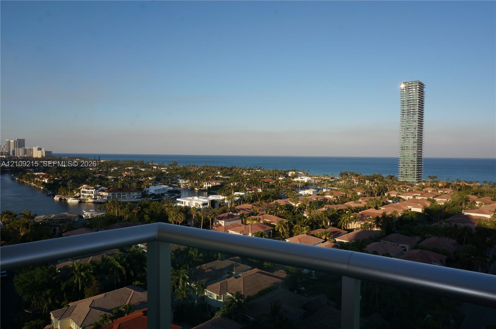 Private balcony with a metal railing, featuring panoramic coastal and cityscape scenery including waterfront areas and high-rise architecture