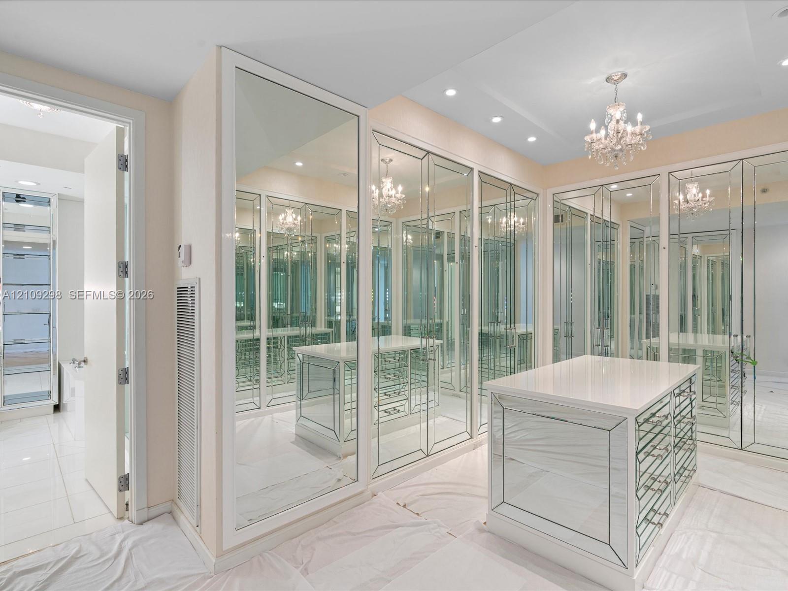 Custom dressing room featuring floor-to-ceiling mirrored cabinetry, a central storage island with integrated drawers, recessed lighting, and a crystal chandelier