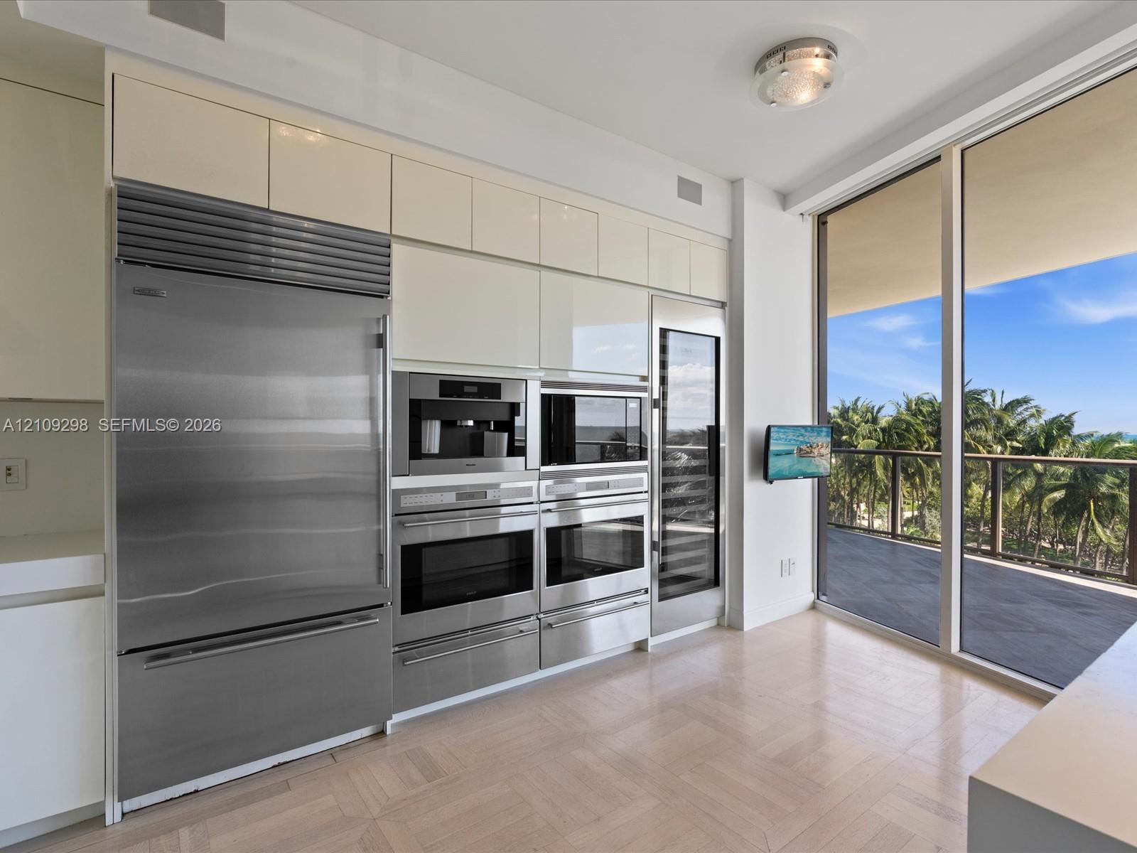 Kitchen featuring high-gloss cabinetry, stainless steel professional-grade appliances, built-in coffee station, integrated wine refrigeration, and floor-to-ceiling glass paneling
