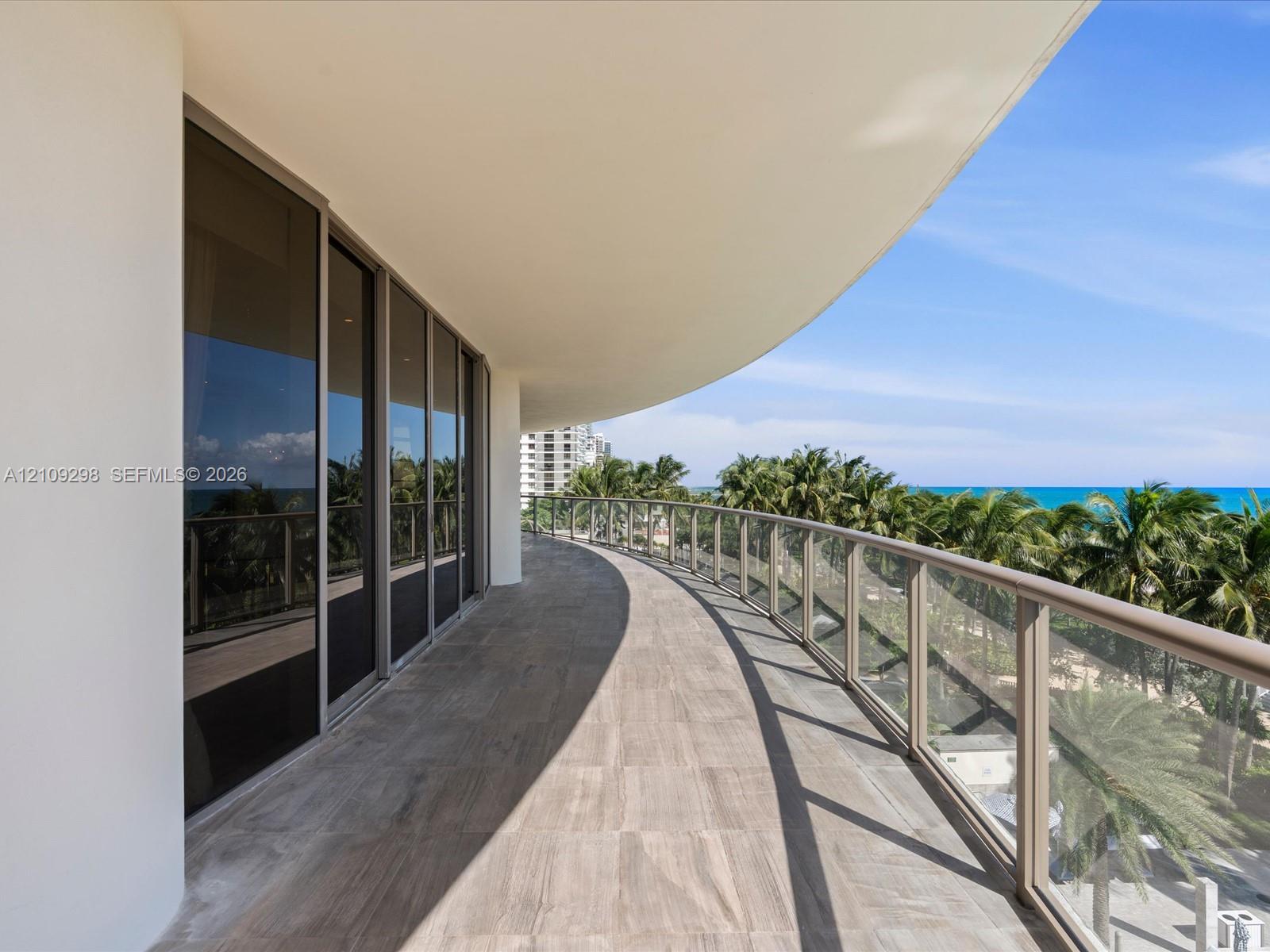 Curved private terrace featuring tile flooring, glass panel railing, and full-height sliding glass doors