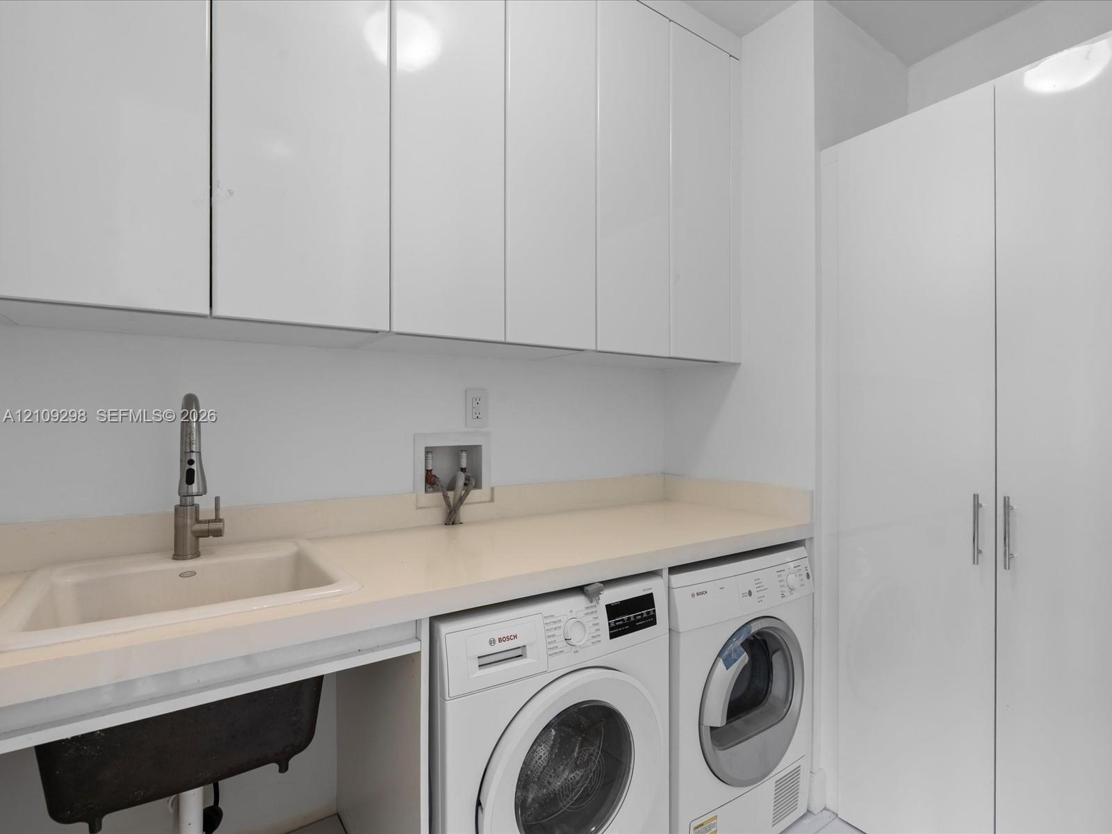 Laundry area featuring high-gloss white cabinetry, a neutral solid-surface countertop, an undermount sink with a gooseneck faucet, and integrated appliance hookups