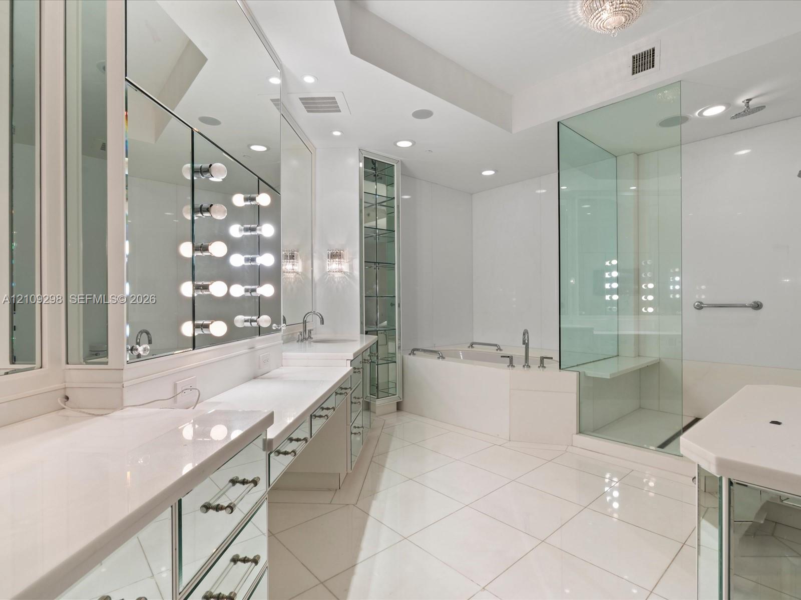 Bathroom featuring expansive vanity with mirrored cabinetry, built-in glass shelving, deep soaking tub, and a frameless glass-enclosed shower with built-in bench