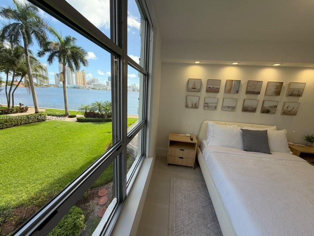 Floor-to-ceiling windows, recessed lighting, and water-facing scenery featuring manicured landscaping and palms