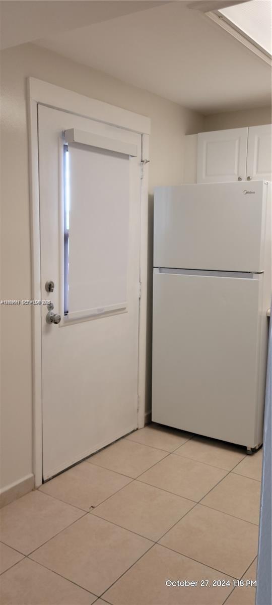 White top-mount refrigerator, neutral ceramic tile flooring, and exterior door with a vertical window insert