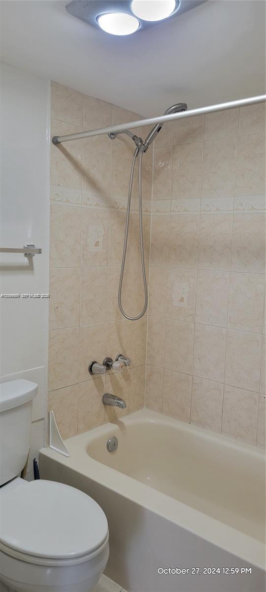 Bathtub and shower combination featuring neutral-toned wall tile, a handheld showerhead, chrome hardware, and an overhead flush-mount light fixture