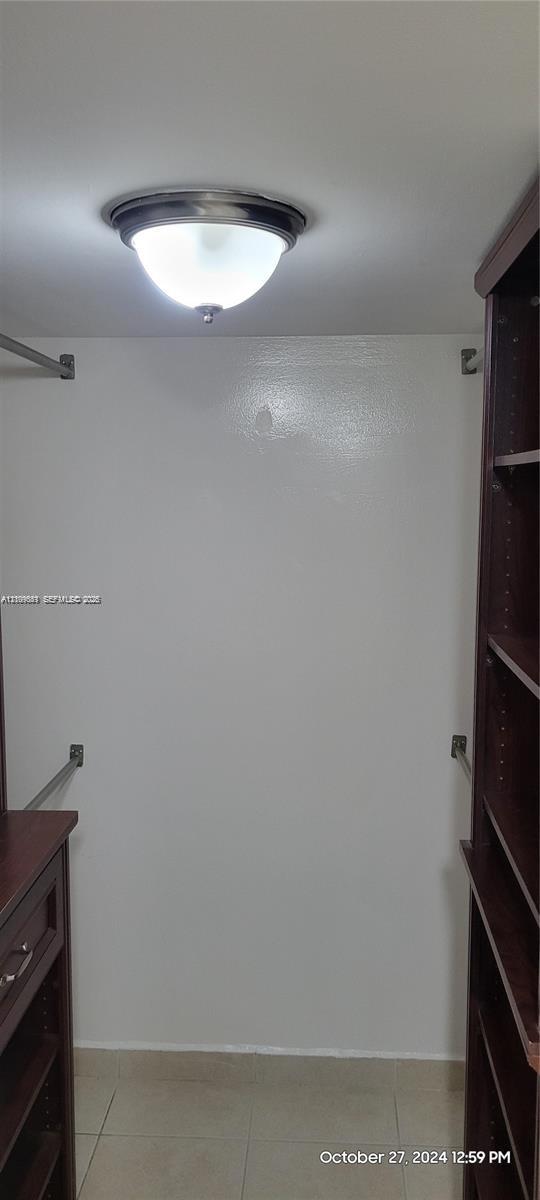 Walk-in closet featuring dark wood-finish built-in shelving, integrated drawers, metal hanging rods, and a ceiling-mounted dome light fixture