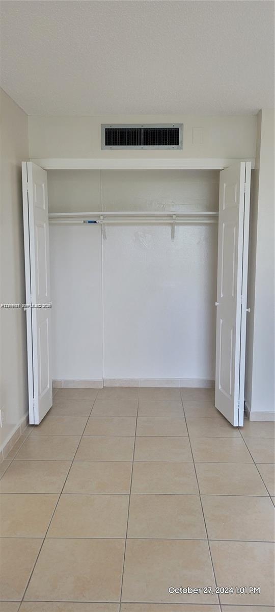 Closet featuring dual folding doors, a built-in overhead shelf, and tile flooring