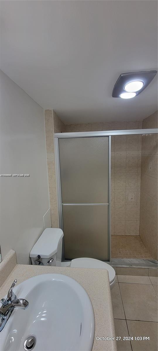Bathroom featuring a vanity with an integrated basin, a walk-in shower with a sliding frosted glass door, tile wall surround, and ceiling-mounted flush light fixture
