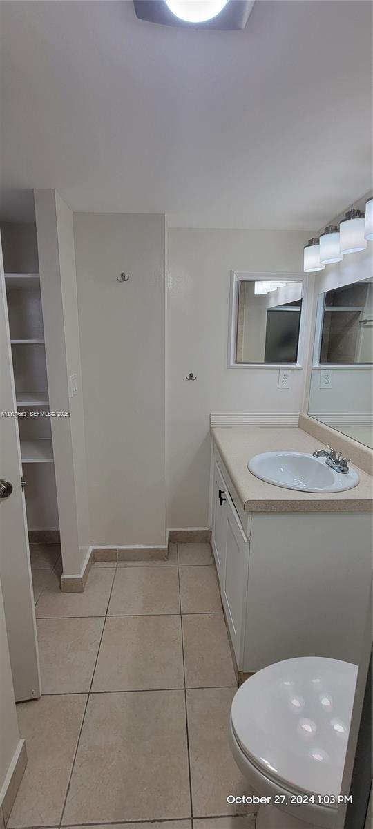 Vanity cabinet with integrated solid-surface countertop and drop-in basin, tiled flooring, wall-mounted mirror, built-in shelving unit, and multi-light fixture