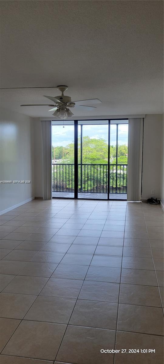 Large interior area featuring light-toned tile flooring, ceiling fan with integrated lighting, and expansive floor-to-ceiling sliding glass doors opening to a private balcony with metal railing