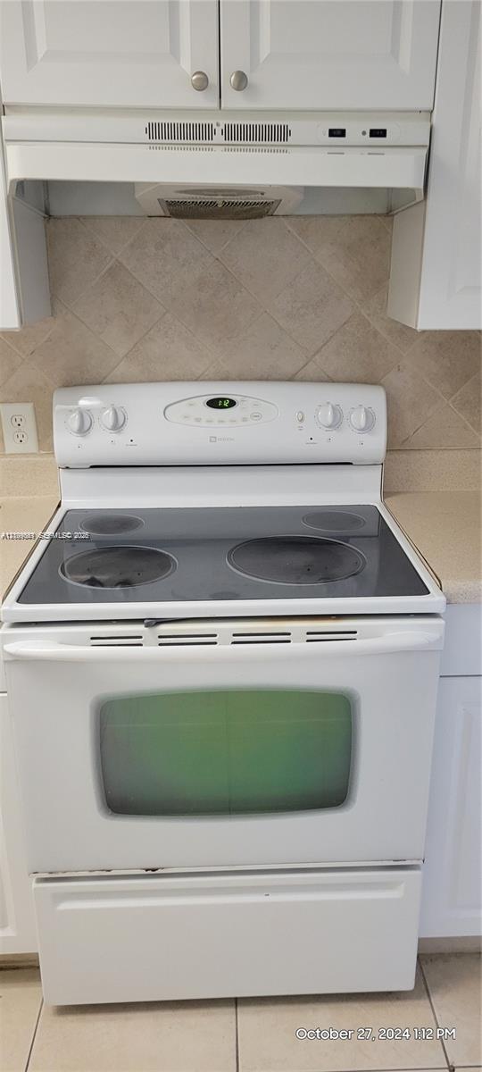 White freestanding electric range with glass cooktop, coordinating over-the-range microwave, white shaker-style upper cabinetry, and a neutral tile backsplash
