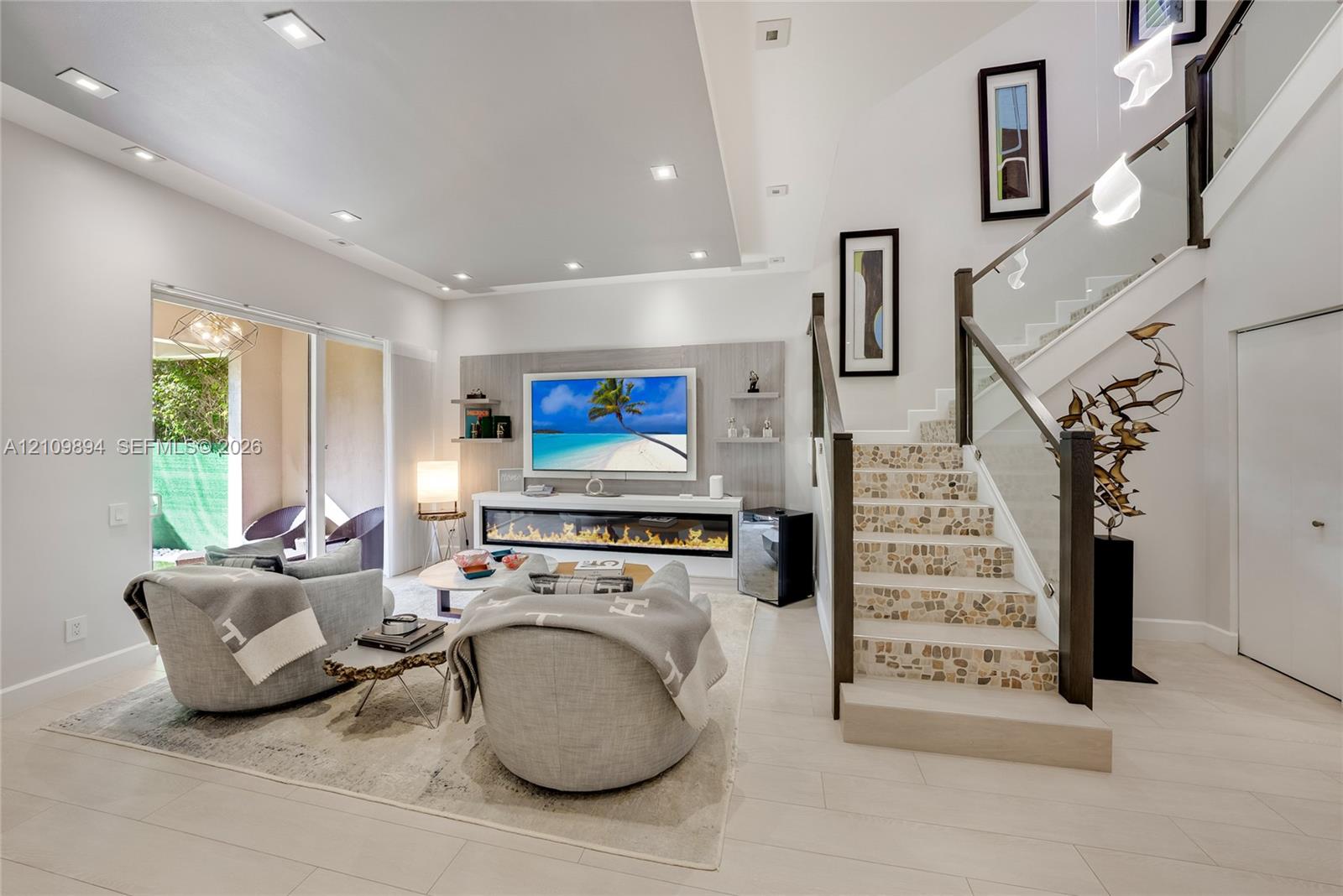 Staircase featuring wood-finish treads, glass balustrades with dark wood handrails, wood-finish flooring, white plantation shutters, and a suspended multi-light fixture