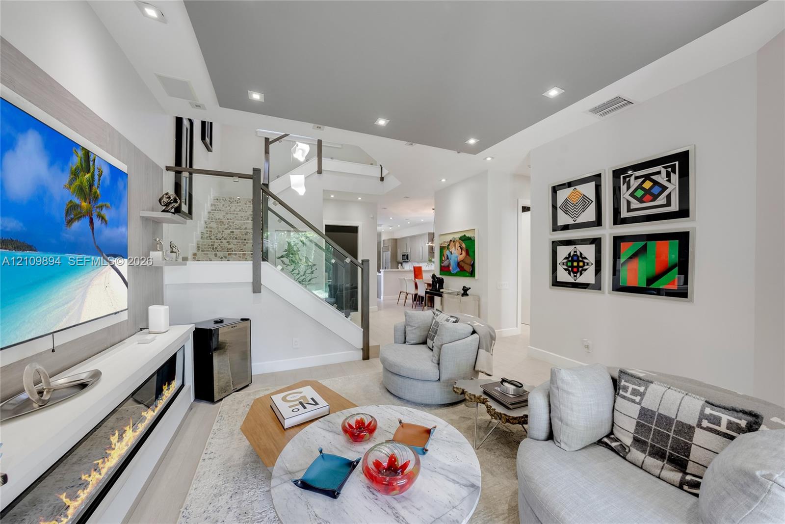 Open-concept living space featuring high ceilings, neutral-toned flooring, glass panel stair railing, and recessed lighting