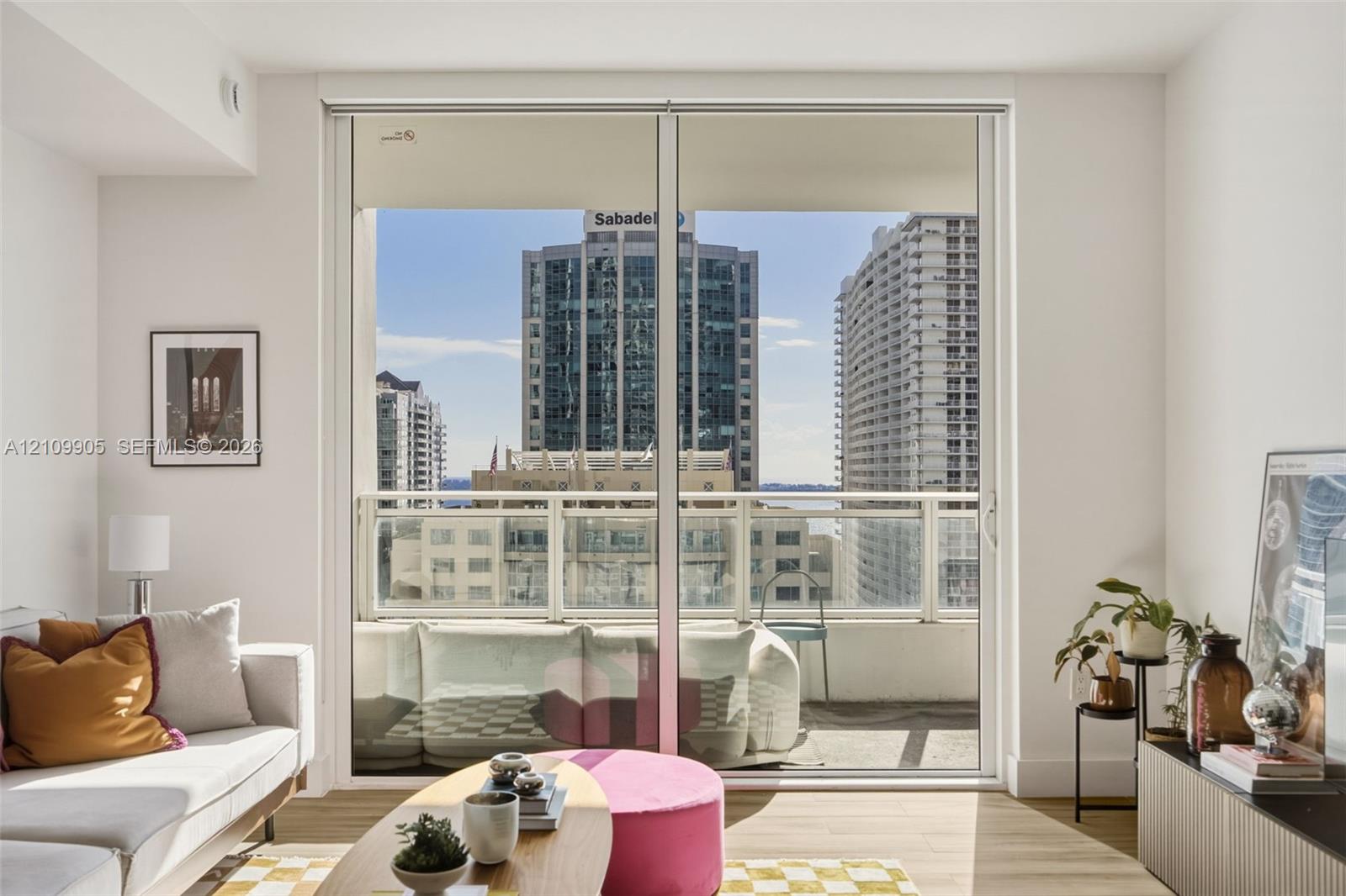 Floor-to-ceiling glass sliding doors opening to an exterior balcony with a glass panel railing and cityscape backdrop