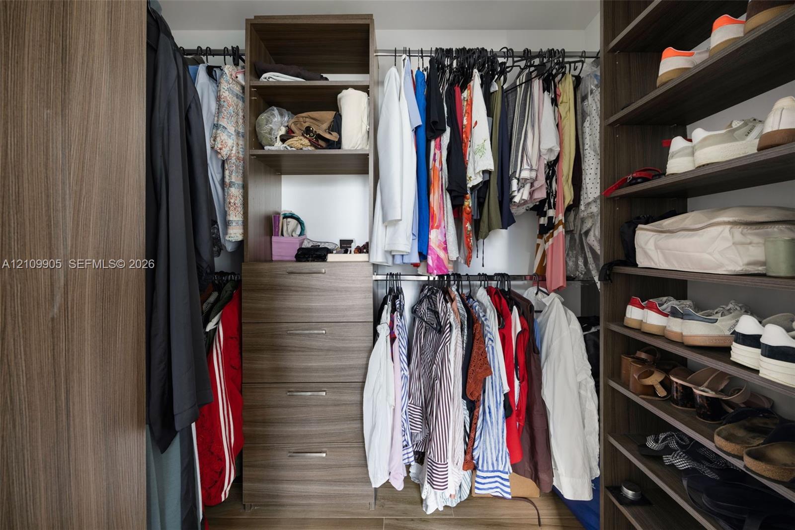 Custom closet organization system featuring wood-finish laminate cabinetry, four integrated storage drawers, adjustable open shelving, and dual-level hanging rods