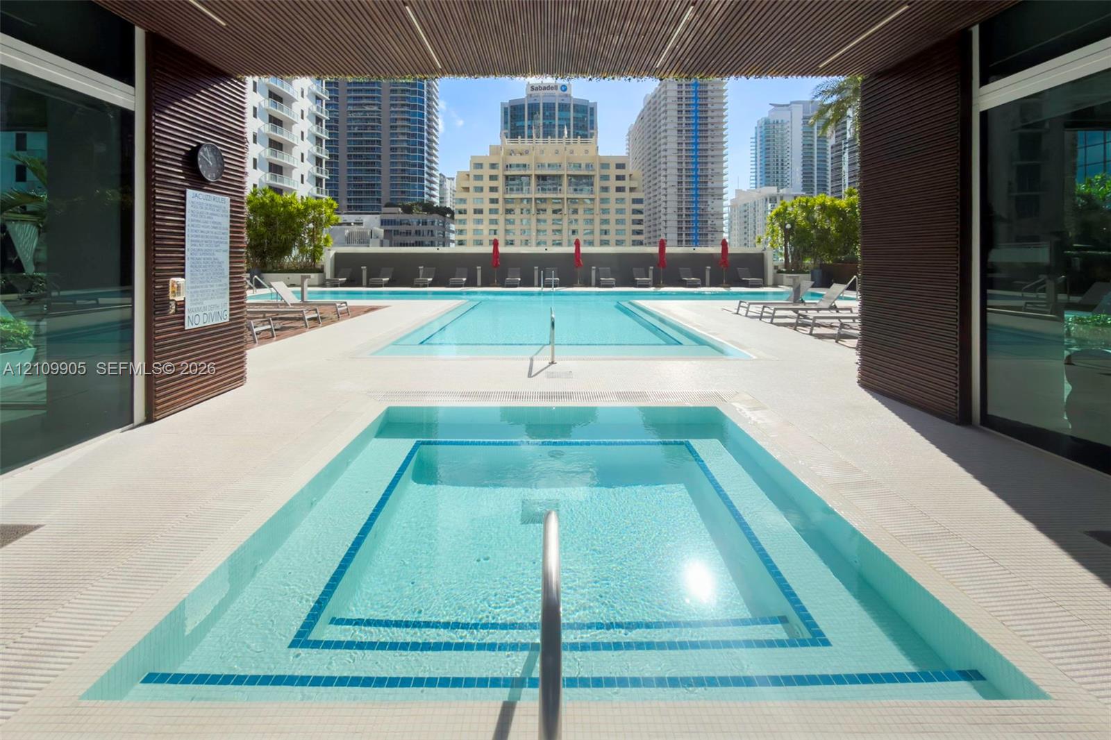 Outdoor terrace featuring a swimming pool, a square spa, horizontal wood-slat ceiling accents, and light-toned tile decking