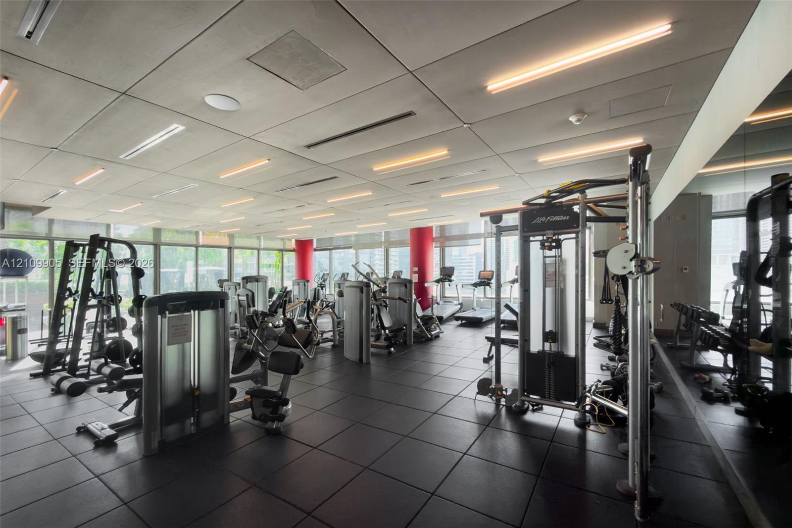Fitness center featuring floor-to-ceiling windows, integrated linear lighting, a mirrored wall, and specialized rubberized flooring