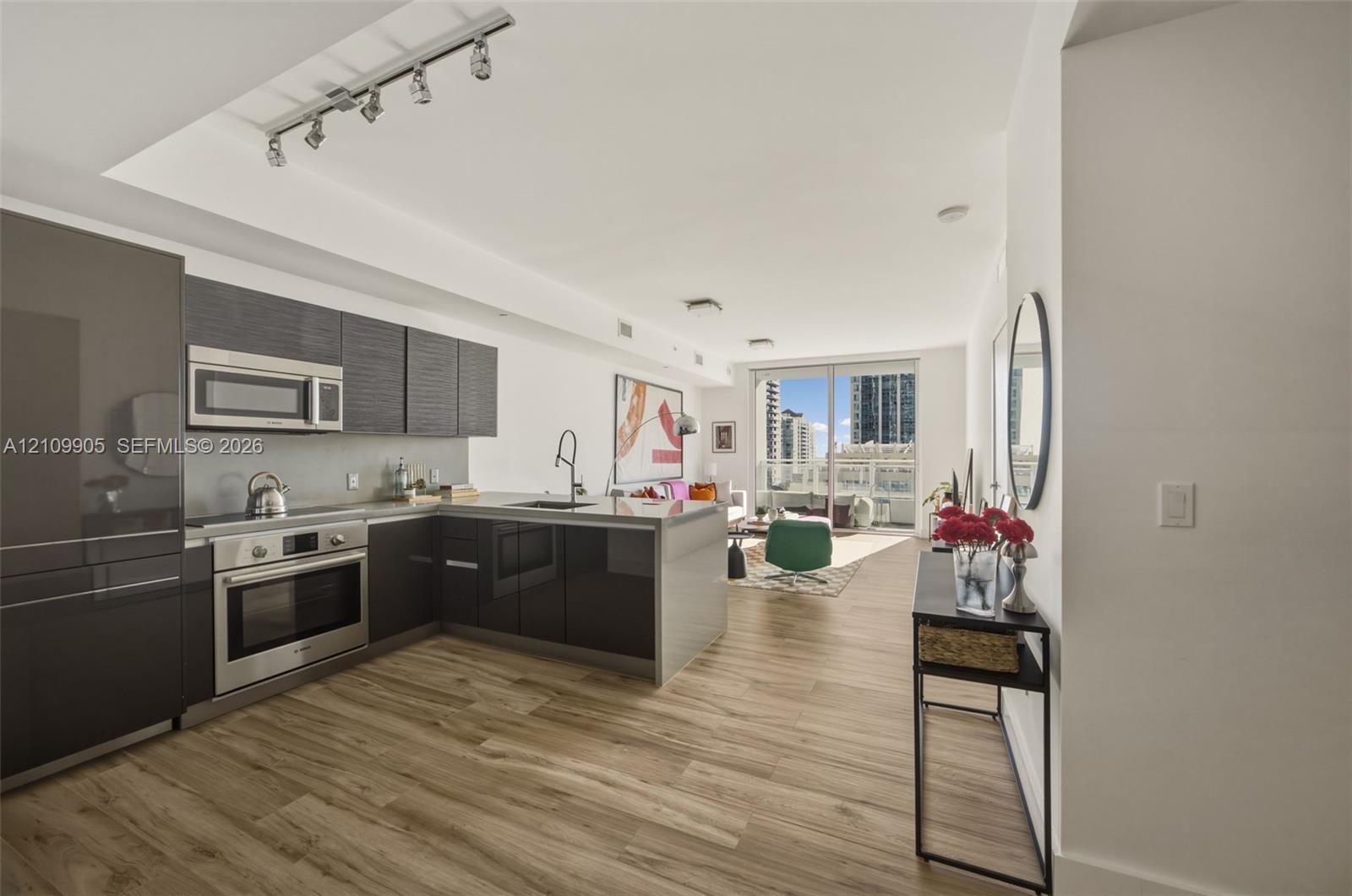 Kitchen featuring high-gloss cabinetry, stainless steel appliances, a peninsula with stone-finish countertops, wood-finish flooring, and recessed track lighting