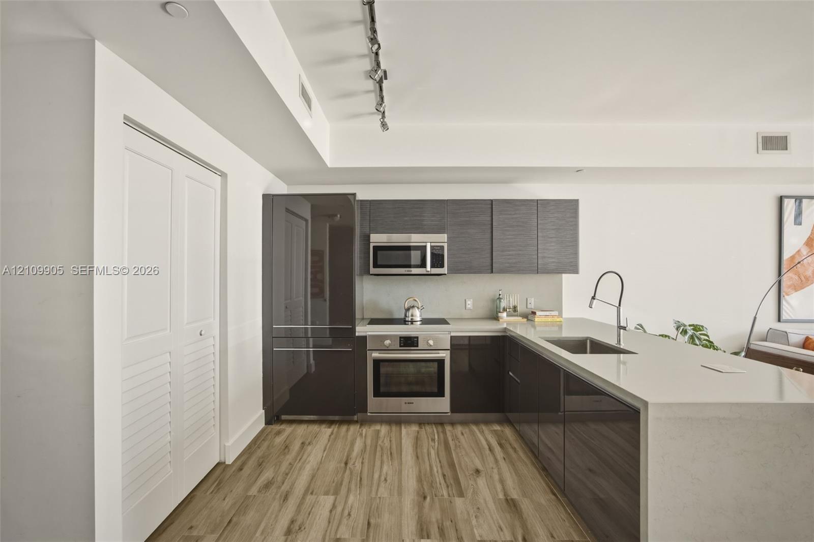 Kitchen featuring high-gloss cabinetry, stone countertops, stainless steel appliances, wood-finish flooring, and industrial track lighting