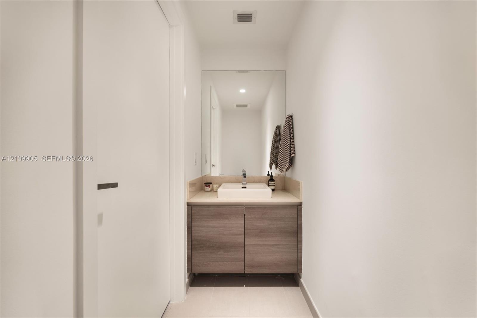 Floating wood-finish vanity with a rectangular vessel sink, neutral stone-finish countertop, and large wall-mounted mirror