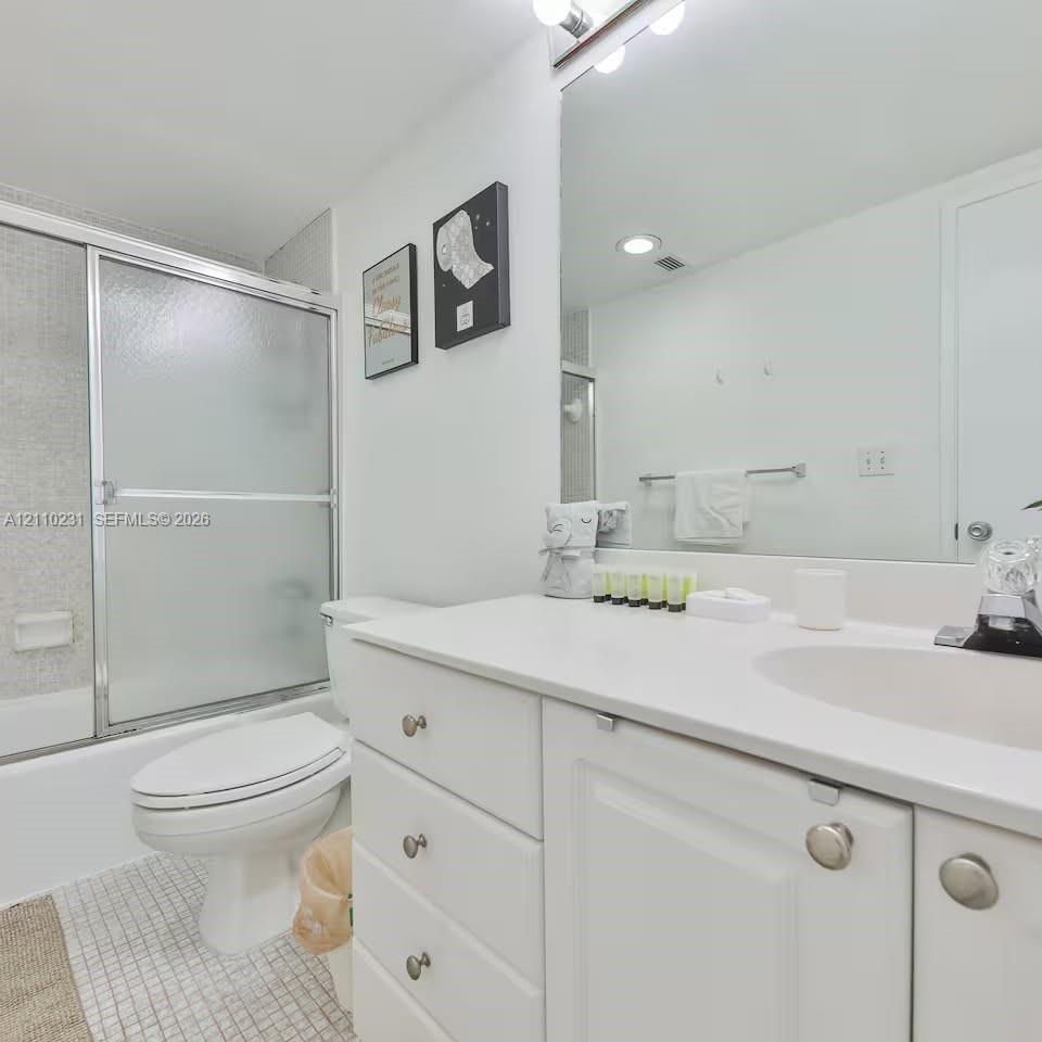 Bathroom featuring a white vanity with integrated basin, polished metal hardware, a wall-spanning mirror, frosted glass sliding shower enclosure, and mosaic floor tile