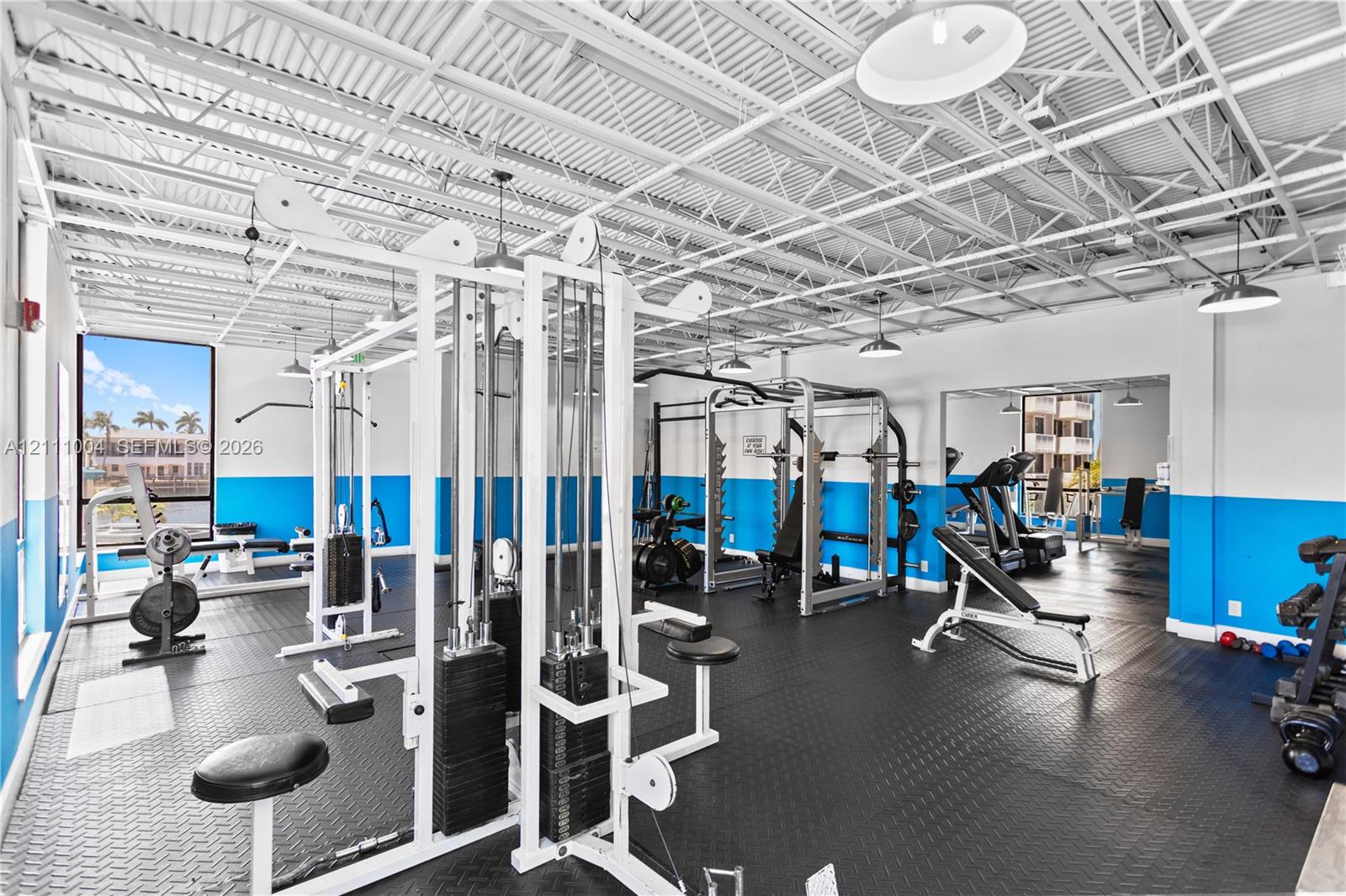 Fitness center featuring exposed truss ceilings, industrial-style lighting, rubberized flooring, and large windows