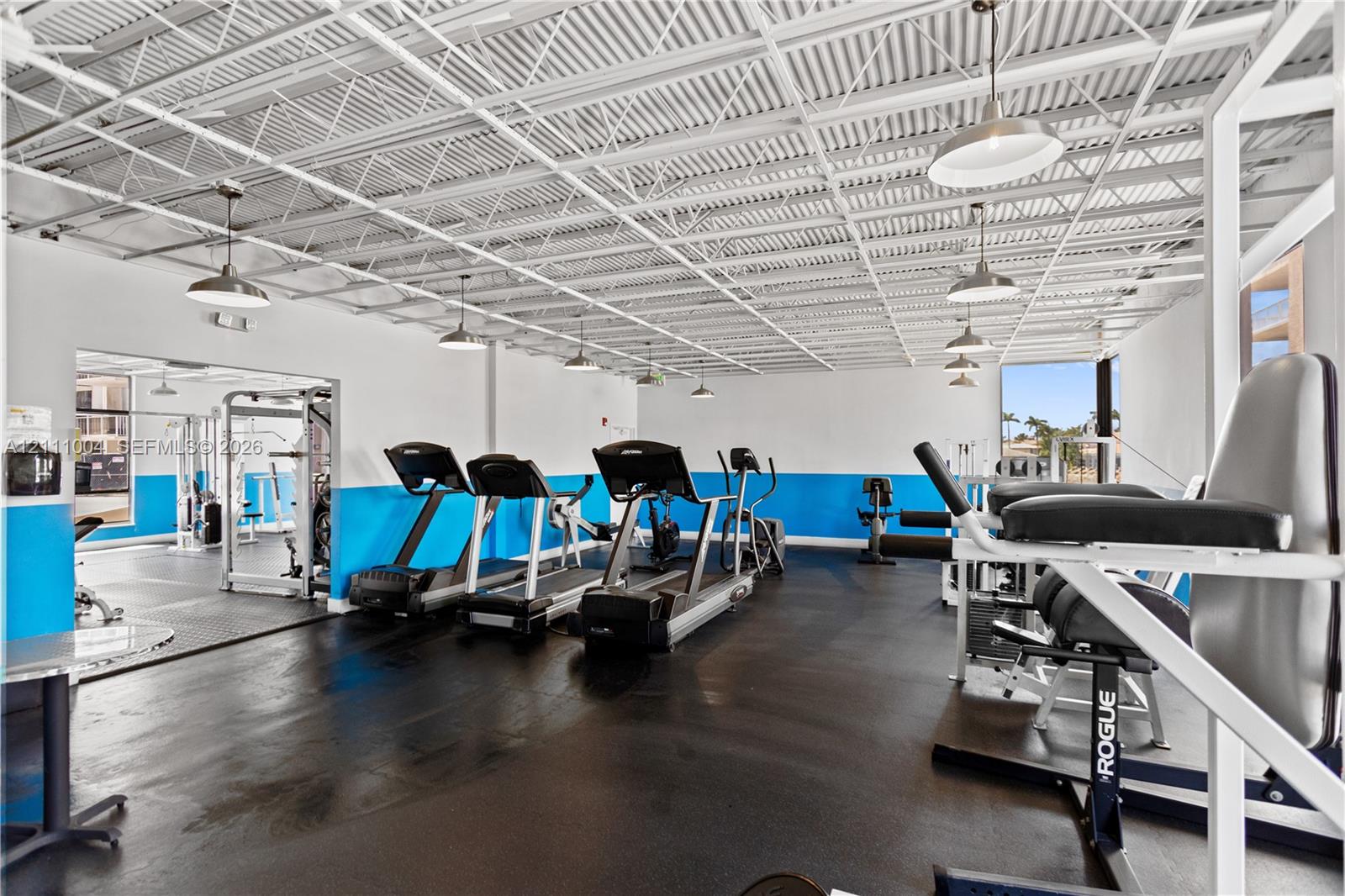 Fitness facility featuring an exposed corrugated metal ceiling, rubberized flooring, pendant lighting, and crisp white and blue wall finishes