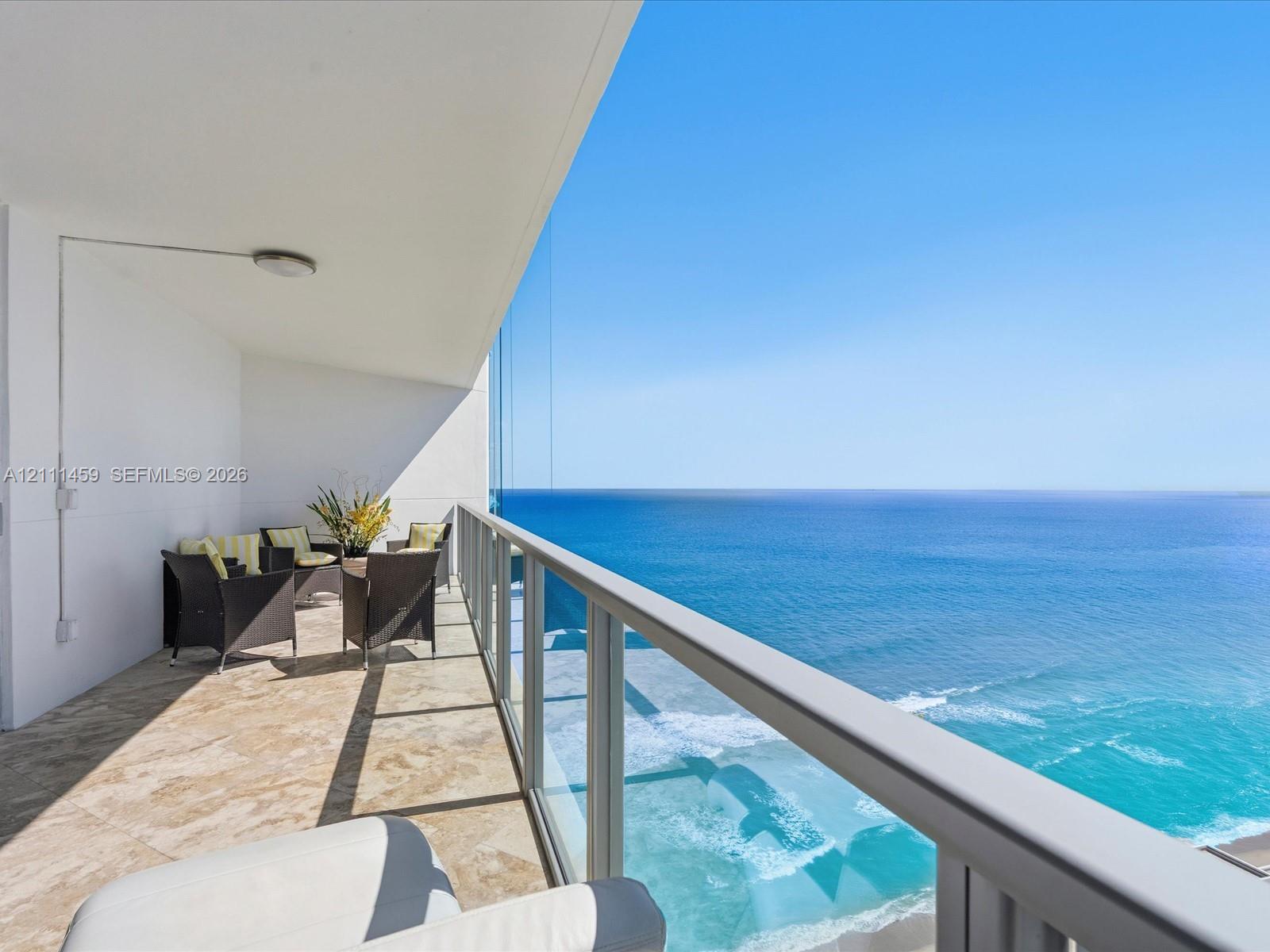 Covered balcony featuring stone flooring and a glass-paneled railing overlooking the ocean