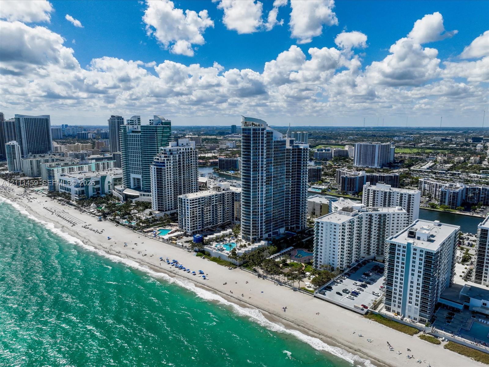 Aerial perspective of a coastal high-rise district featuring direct sandy shoreline access, multiple oceanfront structures, and extensive metropolitan infrastructure
