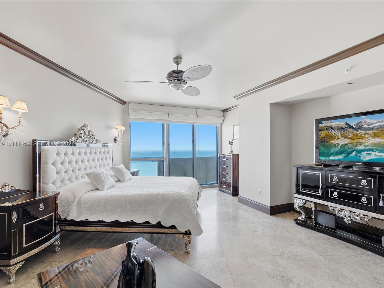 Floor-to-ceiling windows, polished stone flooring, crown molding, wall-mounted light fixtures, and a ceiling fan