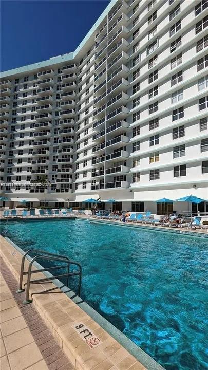 In-ground swimming pool featuring a brick-paver deck and metal ladder access, situated at the base of a high-rise building with multiple private balconies