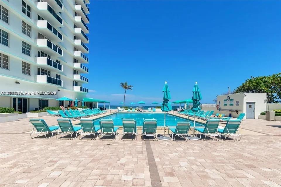 Outdoor swimming pool surrounded by a paved deck featuring a high-rise residential structure