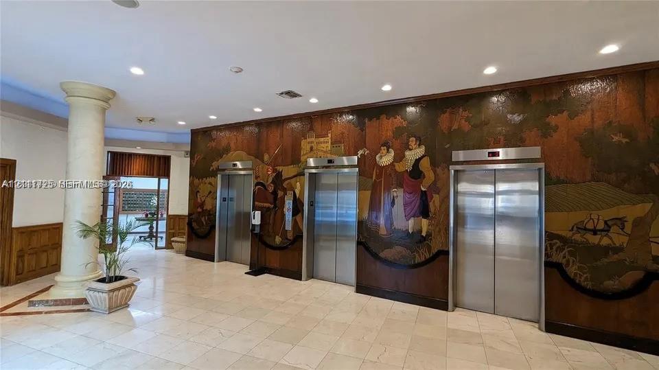 Lobby featuring a large-scale decorative mural, three stainless steel elevator doors, polished stone flooring, and a structural column