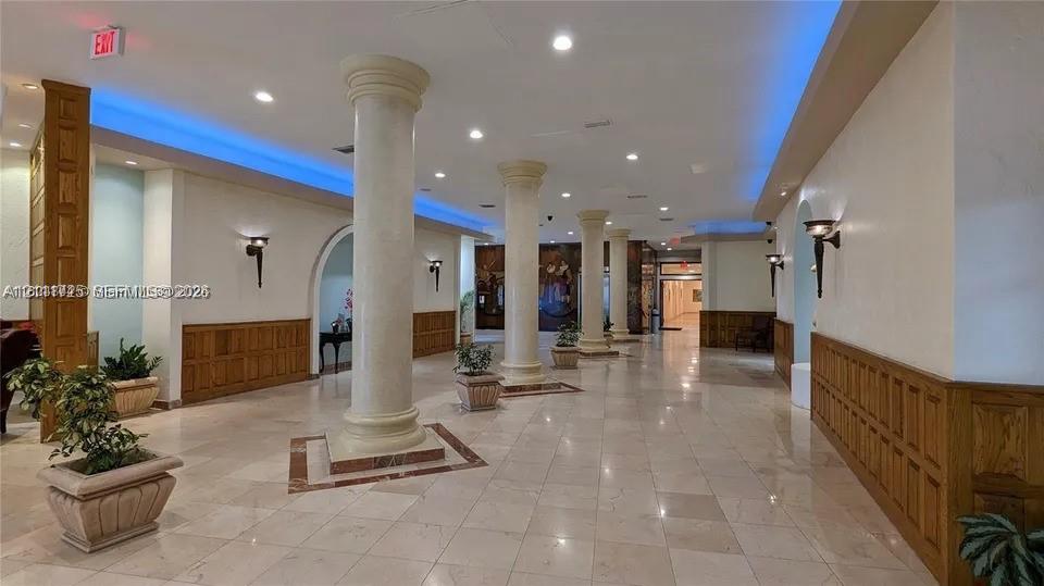 Spacious lobby featuring polished stone flooring, structural columns, recessed lighting, cove accent lighting, and wood paneling