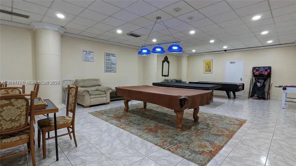 Large recreation room featuring light-colored tile flooring, a suspended drop ceiling, recessed lighting, and a multi-pendant billiards fixture