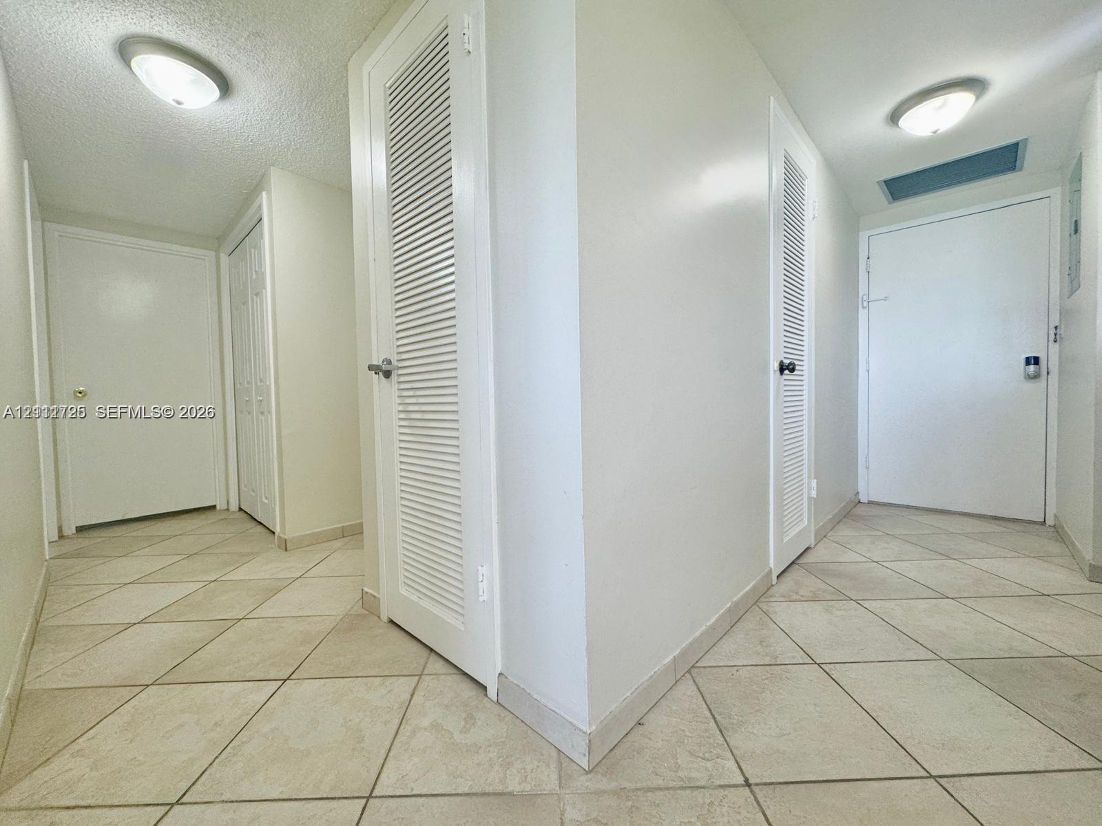 Hallway featuring diagonal tile flooring, flush-mount ceiling lighting, and multiple louvered closet doors